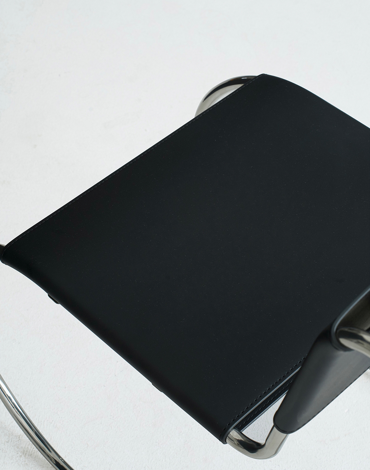 Close-up of a black upholstered chair seat with a curved silver metal frame on a white background.