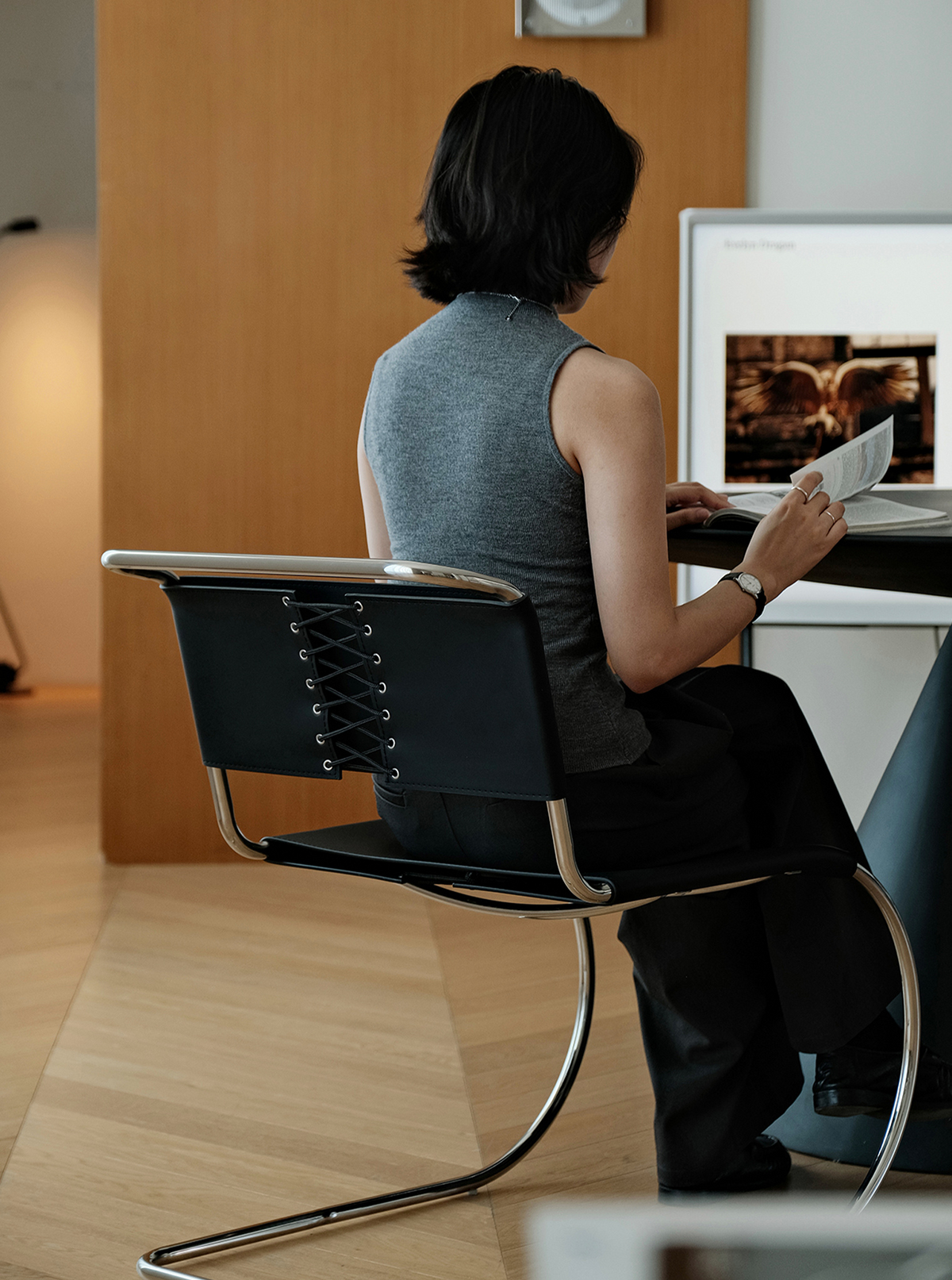 A person seated in a black leather cantilever chair with a chrome curved metal frame, viewed from behind as they sit at a desk in a modern indoor room.