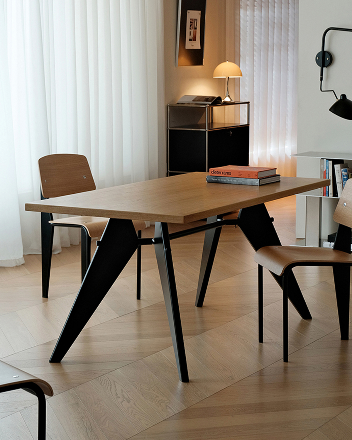 A modern rectangular dining table with a light oak wood top and black angled metal legs, shown in a bright, contemporary room with chairs and curtains.