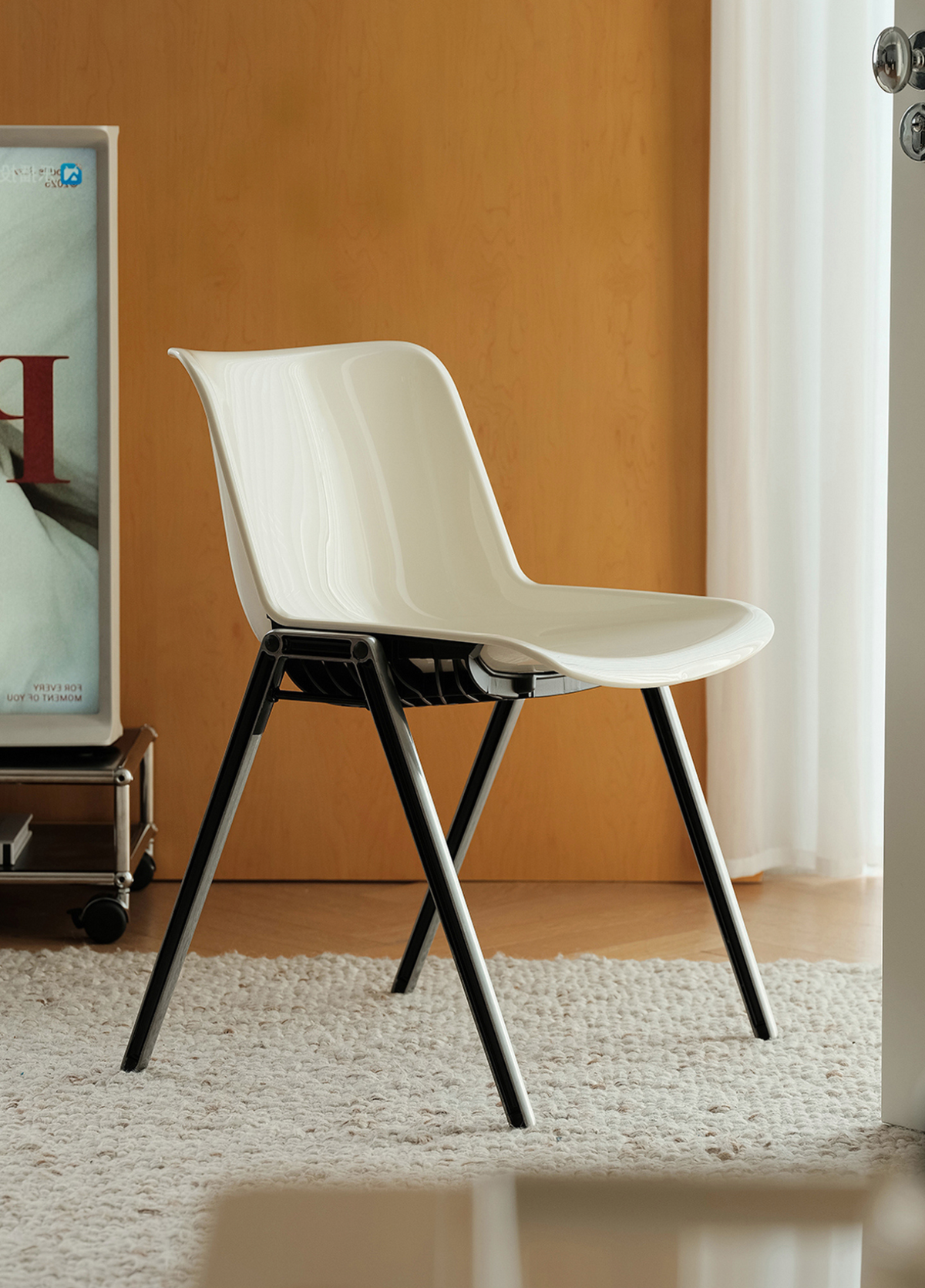 A modern white molded plastic dining chair with black metal legs, positioned on a white shag rug in front of a warm wood-paneled wall.