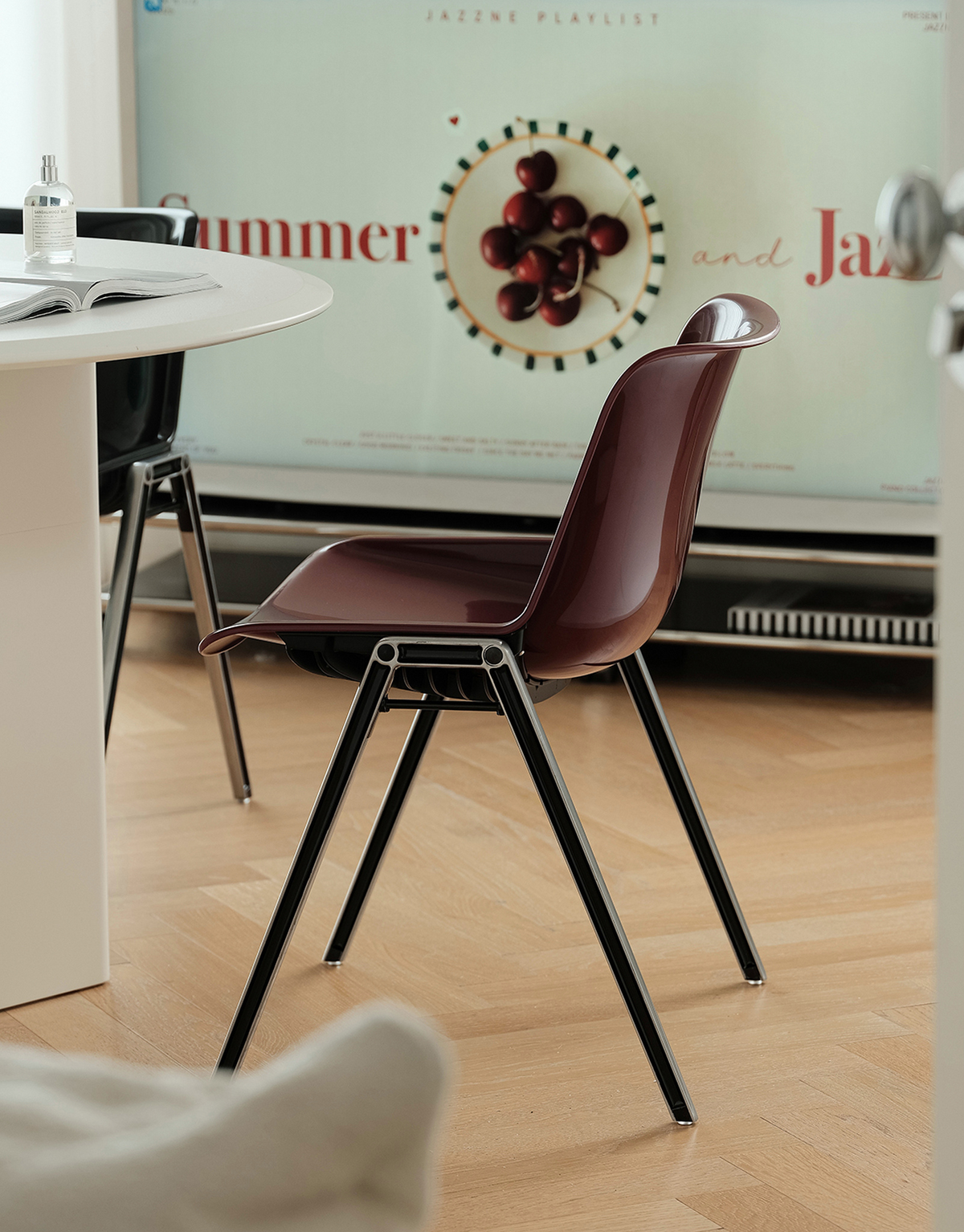 A modern molded plastic chair with a dark reddish-plum seat and back, supported by slim black metal legs, shown in a bright, modern room setting.