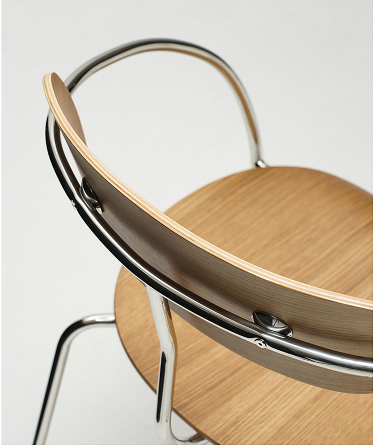 Close-up of a modern wooden chair with a light oak seat and backrest, a curved chrome metal frame, and a thin black outer trim, shown against a light gray background.