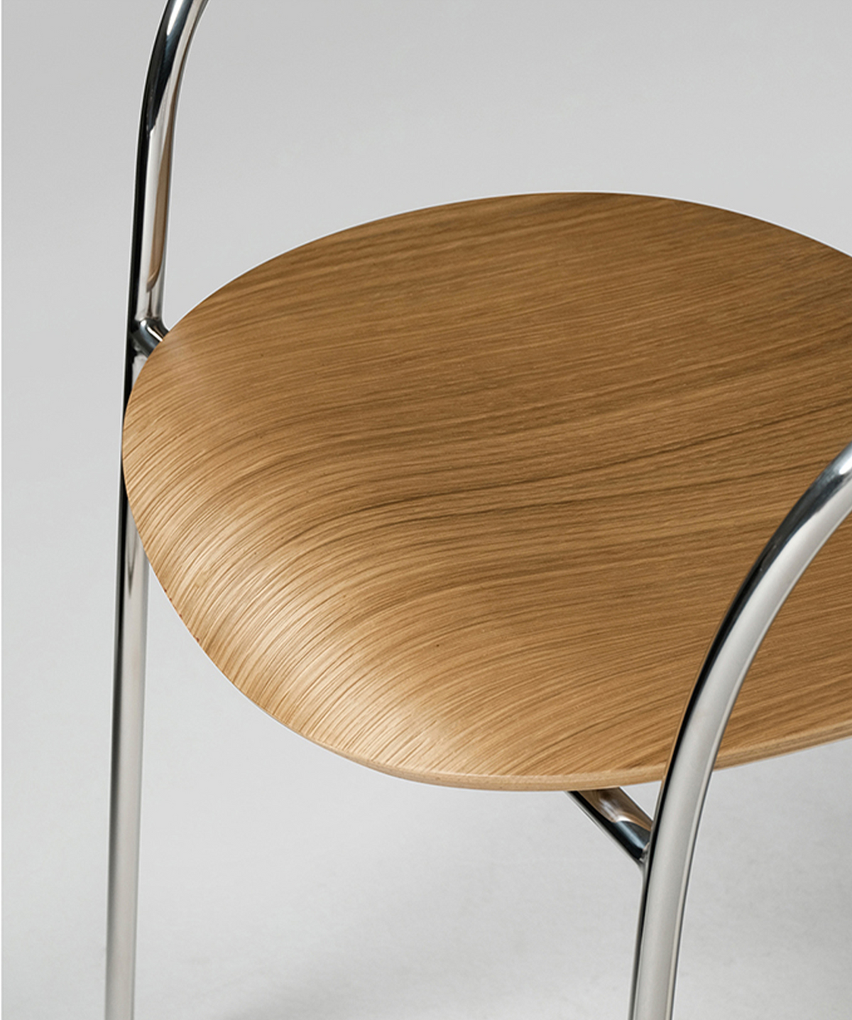 Close-up of a modern chair seat with a light brown wood grain finish and curved polished metal legs on a light gray background.