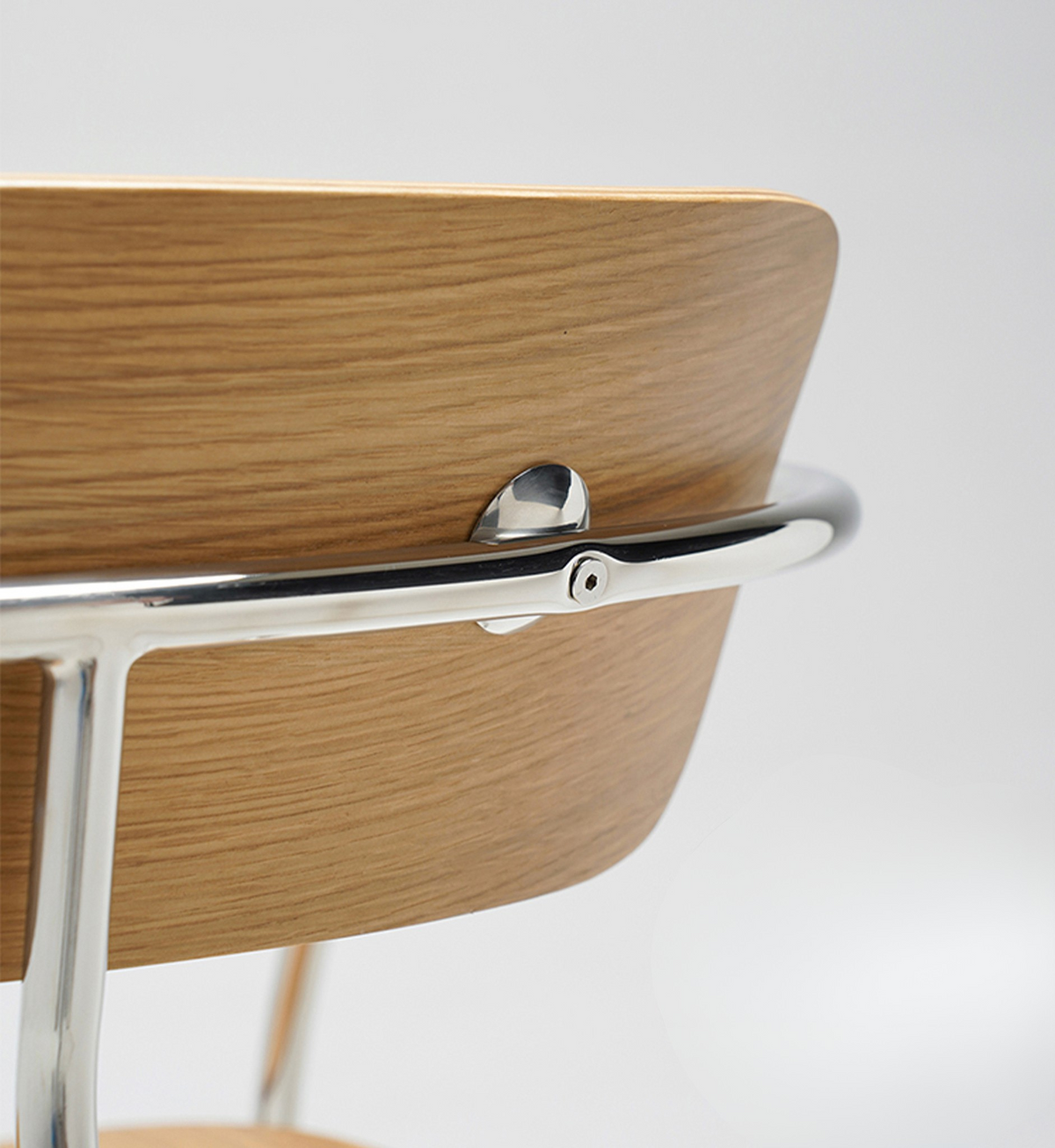 Close-up of a modern chair showing a light oak wood seat back with a polished chrome metal armrest and base.