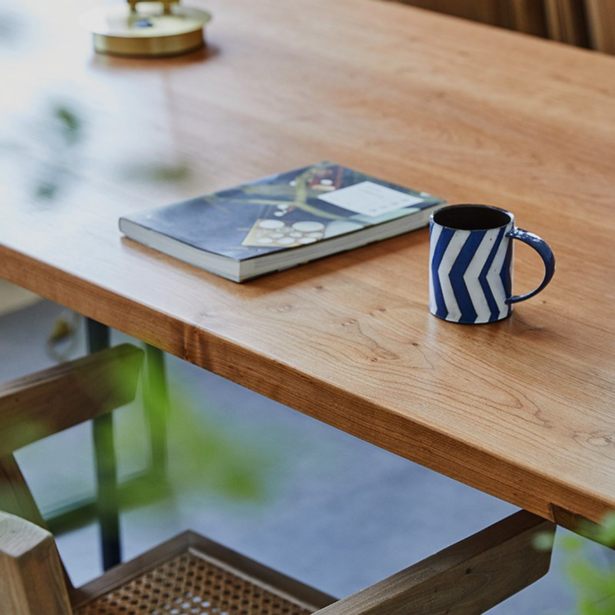 A blue and white chevron-patterned ceramic mug sits on a light brown wooden table next to a book, with a blurred indoor background.