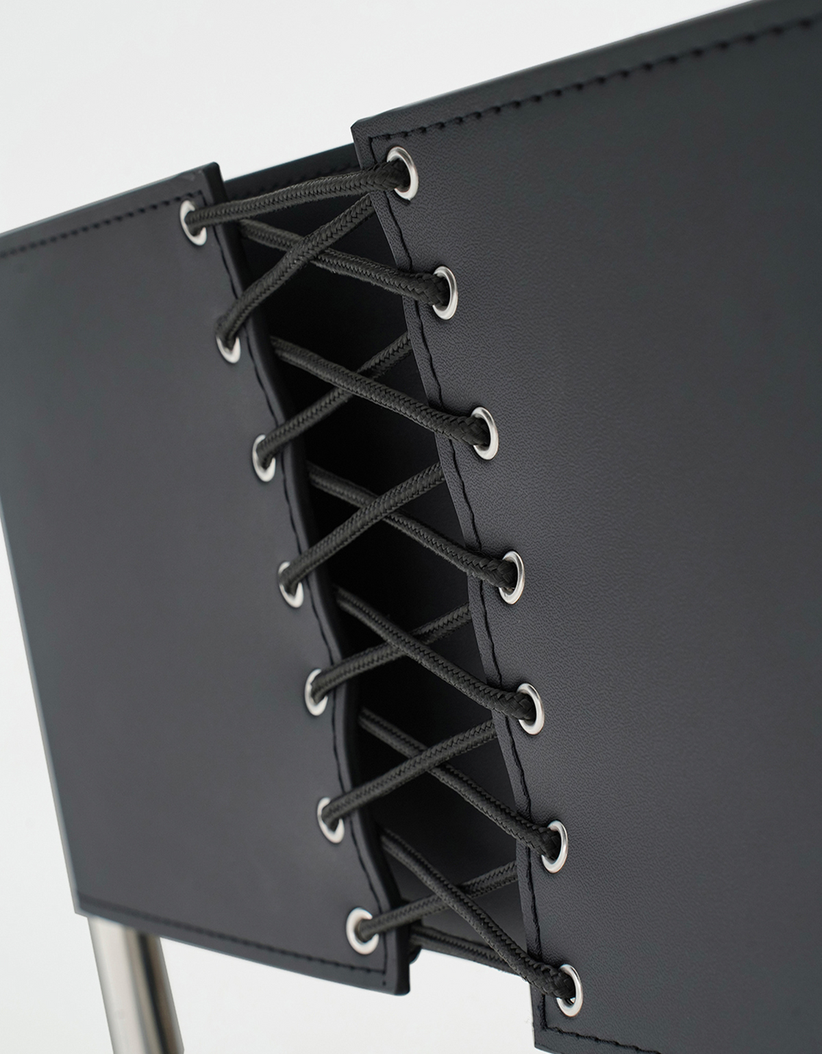 Close-up of a black chair back with a lace-up front panel and silver metal eyelets, shown against a white background.