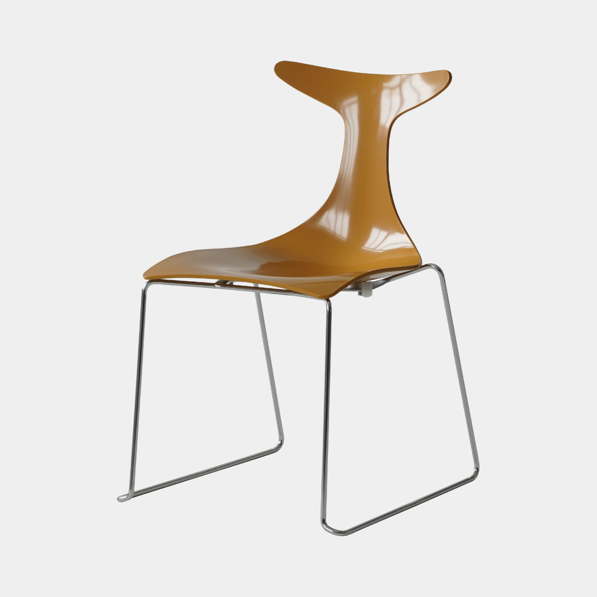 A modern molded plastic chair with a glossy mustard-yellow seat and backrest, supported by a chrome wire frame, shown against a light gray background.