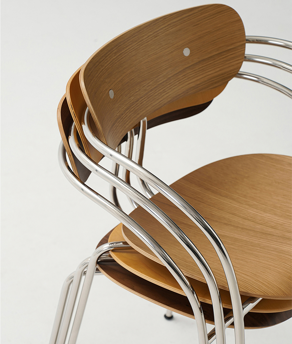 A close-up of a stack of modern wooden dining chairs with curved silver metal tubular frames, set against a plain white background.