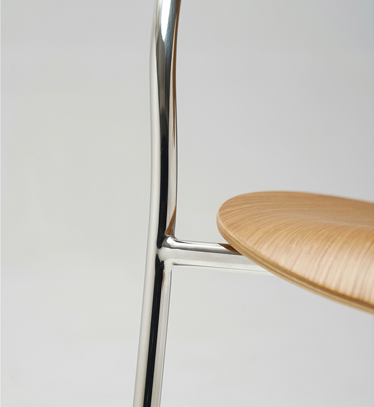 Close-up of a modern chair showing a curved light natural wood seat and a polished chrome metal frame against a light gray background.