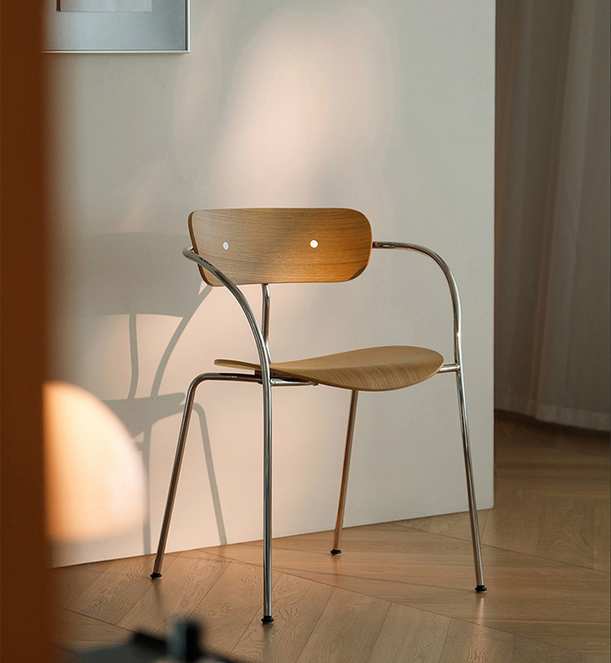 A modern wooden dining chair with a curved chrome metal frame, set against a minimalist beige wall on a light wood parquet floor.